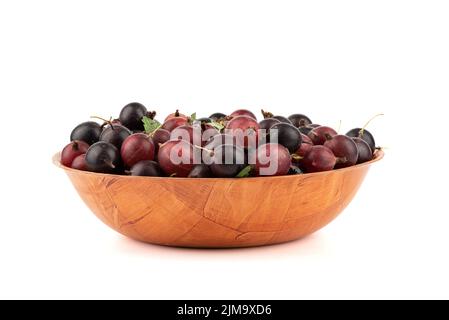 Rote reife Stachelbeeren in einer Holzschale auf weißem Hintergrund. Stachelbeere lat. Ribes uva-crispa ist ein Laubstrauch der Familie der Stachelbeere. Stockfoto