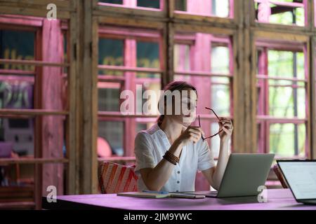Müde junge Angestellte, die eine Brille auszieht, die eine Brille in der Hand hält, die von der Computerarbeit ruht Stockfoto