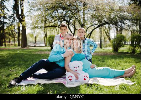 Glücklich schwanger paar mit zwei Söhnen umarmt und sitzen auf karierten Hintergrund Frühling Natur Stockfoto