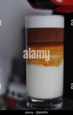 Eine vertikale Nahaufnahme von dreilagiger Latte Macchiato in einem hohen Glas. Stockfoto