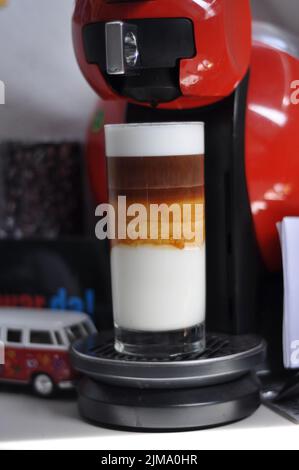 Eine vertikale Nahaufnahme von dreilagiger Latte Macchiato aus einer Dolce Gusto Kapselmaschine. Stockfoto