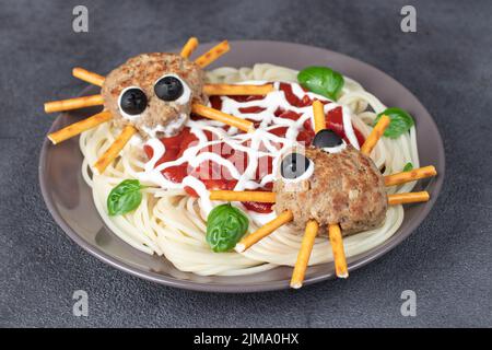 Koteletts sehen aus wie Spinnen mit Oliven und Trinkhalmen, serviert mit Spaghetti-Nudeln und Tomatensauce auf Grau. Halloween-Frühstücksidee Stockfoto