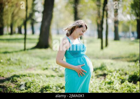 Porträt von glücklich schwangere Frau, gekleidet in einem türkisfarbenen Kleid im park Stockfoto