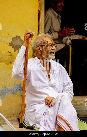 Ein alter indischer Mann in weißen traditionellen Kleidern sitzt an einer gelben Wand, Nathdwara, Indien Stockfoto
