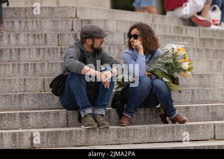 Eine schöne Aufnahme eines verliebten Paares mit einem Blumenstrauß, der auf einer Treppe sitzt Stockfoto