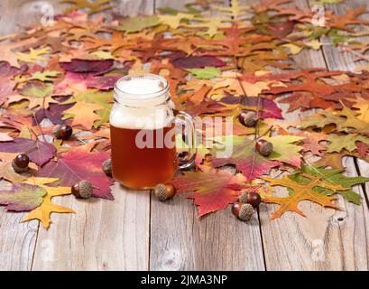 Frisch gezapftes Bier mit Herbstlaub und Eicheln auf rustikalen Holzbrettern Stockfoto