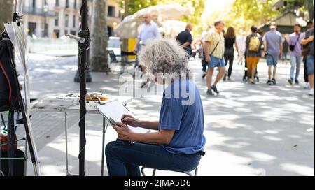 Barcelona, Spanien - 22. Mai 2022: Straßenkünstler malt eine Zeichnung auf Karton auf den ramblas von Barcelona (Spanien), selektiver Fokus auf graues Haar. Stockfoto