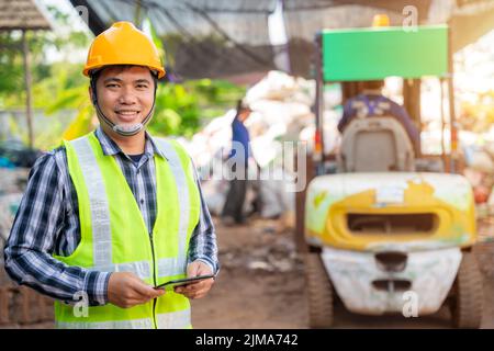 Asiatische Arbeiter in der Recyclingfabrik mit einem Gabelstapler im Hintergrund, Ingenieure im Recyclingzentrum. Abfall recyceln, Müll recyceln. Stockfoto