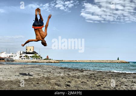 Ein junger Mann, der Backflips macht, wirft Saltos in den Sand. Stockfoto