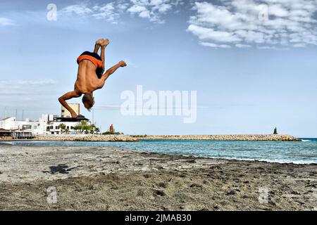 Ein junger Mann, der Backflips macht, wirft Saltos in den Sand. Stockfoto