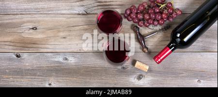 Öffnen Sie eine Flasche Rotwein und Gläser mit Trauben auf rustikalen Holzbrettern Stockfoto