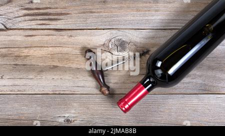 Öffnen Sie eine Flasche Rotwein mit Vintage-Korkenzieher auf rustikalen Holzbrettern Stockfoto