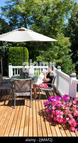 Junger Mann, der seinen Hund umarmt, während er von zu Hause aus auf seinem Zederndeck arbeitet Stockfoto