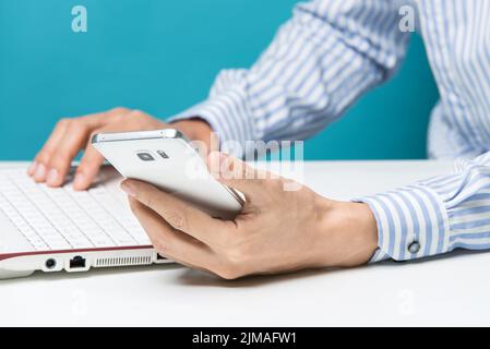 Männliche Hände, Notebooks und Smartphones für Unternehmen im Büro auf blauem Hintergrund Stockfoto