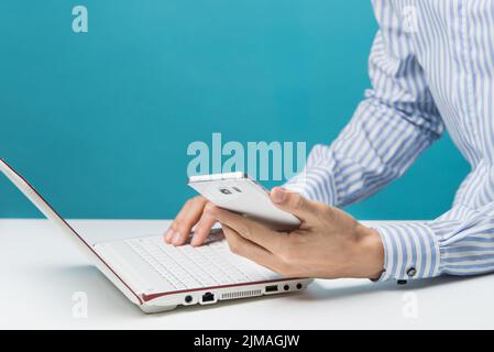 Männliche Hände, Notebooks und Smartphones für Unternehmen im Büro auf blauem Hintergrund Stockfoto