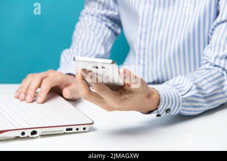 Männliche Hände, Notebooks und Smartphones für Unternehmen im Büro auf blauem Hintergrund Stockfoto