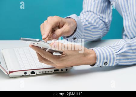 Männliche Hände, Notebooks und Smartphones für Unternehmen im Büro auf blauem Hintergrund Stockfoto