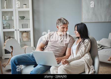 Ehemann und Ehefrau, die in ihrem Wohnzimmer einen Laptop benutzen. Stockfoto