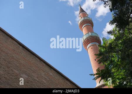 Blick auf Minarett, Eckansicht der Moschee im Zentrum von Konya, Minarett aus roten Ziegeln über grünem Baum. Stockfoto