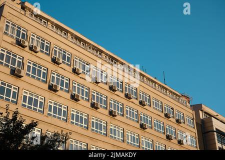 Regierungsgebäude in Diyarbakir. Sonnenlichtreflexion an der Fassade der Wand. Viele Klimaanlagen hängen an Wand und Fenster. Stockfoto