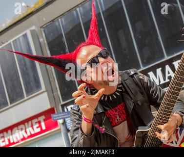 Little John Guelfi a Busker, Musikkünstler, Punk-Rock- und Metal-Straßenmusiker in Blackpool, Lancashire, Großbritannien. August 2022. Die Punk-Subkultur, Ideologien, Mode, mit Mohican gefärbten Frisuren und Farbstoffen beim Punk Rebellion Festival in den Winter Gardens. Ein Protest gegen konventionelle Einstellungen und Verhaltensweisen, ein Zusammenprall von Anti-Establishment-Kulturen, Mohawks, Sicherheitsnadeln und eine Menge Haltung in der Küstenstadt, da Punks, die das jährliche Rebellion Rock Music Festival in den Wintergärten besuchen, mit traditionellen Urlaubern Seite an Seite stehen. Stockfoto