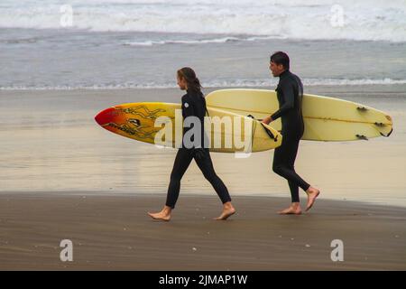 Ein Blick auf ein Paar in Neoprenanzügen mit Surfbrettern am Strand, die sich zum Surfen vorbereiten Stockfoto