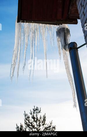 Große Eiszapfen hängen von dem Dach des Hauses gegen den Himmel Stockfoto