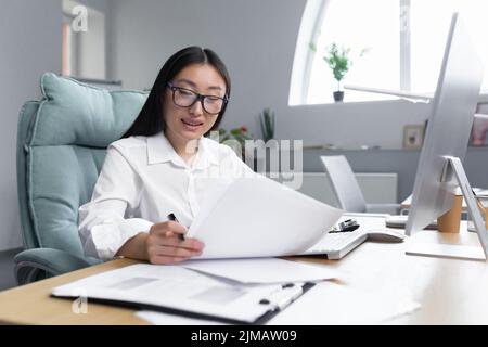 Arbeiten mit Dokumenten. Porträt einer jungen schönen Geschäftsfrau Asiatische Buchhalterin arbeitet mit Dokumenten und Berichten. Am Schreibtisch im Büro sitzen und schreiben. Stockfoto