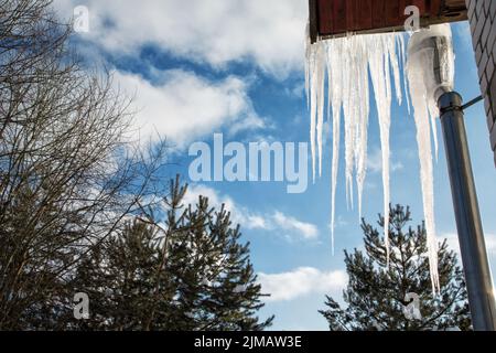 Große Eiszapfen hängen von dem Dach des Hauses gegen den Himmel Stockfoto