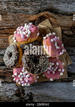 Leckere gebackene glasierte und Schokoladendonuts auf einem Holzbrett isoliert. Rosa, braun und schwarz. Warme Atmosphäre. Stockfoto