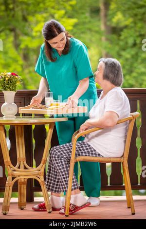 Krankenschwester, die einer glücklichen älteren Frau ein gesundes Frühstück serviert Stockfoto