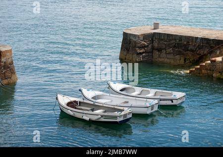 Drei weiße Boote, die in blauem Wasser schwimmen, vertäut im Hafen von Coliemore in Dalkey, Republik Irland. Sonniger Sommertag. Stockfoto