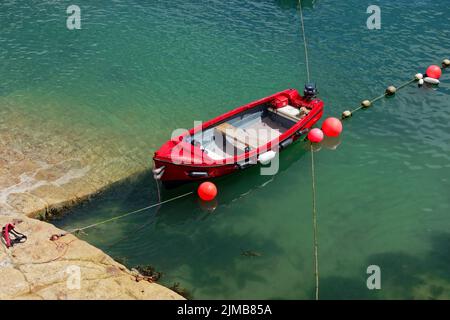 Rotes Boot, das am heißen Sommertag im Hafen von Coliemore festgemacht wurde. Farben und türkisfarbenes Wasser lassen das Bild wie im Mittelmeer aufgenommen erscheinen. Stockfoto