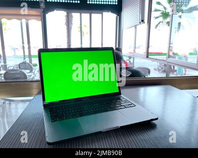 Ein Mockup-Bild des Laptops mit leerem grünen Bildschirm auf dem Tisch Stockfoto