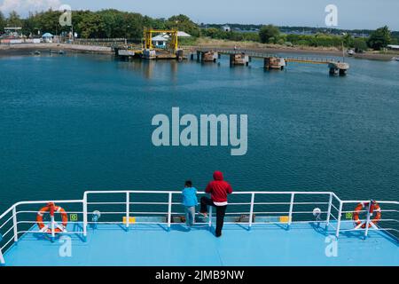 Kayangan, Nord-Lombok, Indonesien - 9. Juli 2022: Vater und Sohn, die am Hafen von der Seite des Fährschiffs, das andocken wird, die Hauptrolle spielen Stockfoto