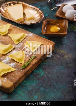 Zubereitung von traditionellen italienischen Ravioli gefüllt mit Hackfleisch. Ravioli auf einem Holzschneidebrett auf Marmorboden. Knödel mit Fleisch, ra Stockfoto