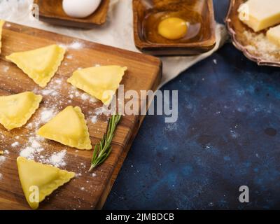 Appetitliche Ravioli auf einem Schneidebrett und Zutaten auf blauem Marmorboden. Italienische Küche Rezepte, Restaurant und Hausmannskost, Rezeptbuch, Stockfoto