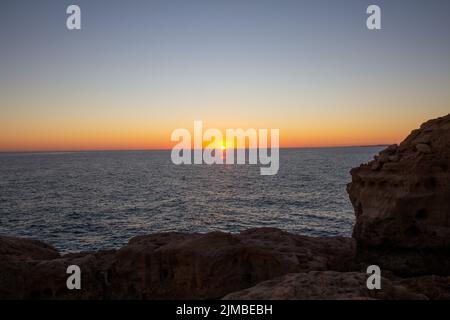 Ein atemberaubender Sonnenuntergang mit der hellen Sonne, die in einem orangefarbenen Himmel über dem Strand der Algarve, Portugal, scheint Stockfoto