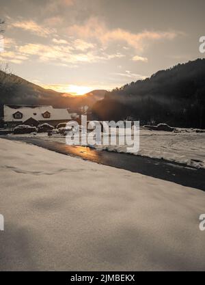 Fantastische abendliche Winterlandschaft, die durch Sonnenlicht leuchtet. Dramatische winterliche Szene bei Sonnenuntergang Stockfoto