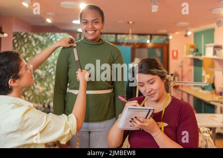 Team von Mitarbeitern, die die Messungen eines Kunden in einer Nähwerkstatt niederschreiben Stockfoto