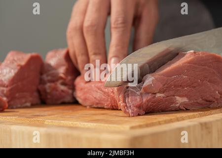 Nahaufnahme eines Mannes, der mit einem Messer auf einem Holzbrett Fleisch in Stücke schneidet Stockfoto
