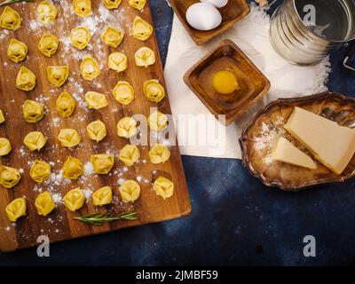 Der Prozess der Küche köstliche hausgemachte Knödel, Ravioli. Kleine Knödel auf einem Schneidebrett, Zutaten auf blauem Marmorboden. Viele Obj Stockfoto