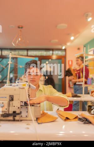 Vertikales Foto einer jungen kaukasischen Frau mit kurzen Haaren, die in einer Nähwerkstatt arbeitet Stockfoto