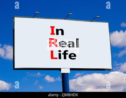 IRL im realen Leben Symbol. Konzeptwörter IRL im wirklichen Leben auf weißer Plakatwand gegen blauen Himmel und Wolken. Schöner Hintergrund. Business und IRL in Real Stockfoto