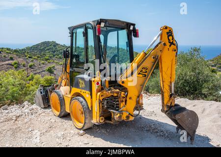 Kleiner JCB-Bagger mit Eimer auf einer Baustelle an der Küste auf einem Hügel nahe dem Meer auf der griechischen Insel Zante oder zakynthos in griechenland. Stockfoto