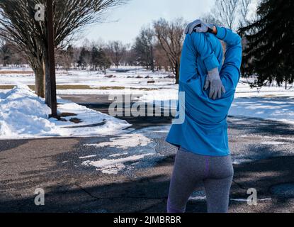 Die Frau wärmte sich auf und streckte ihre Arme vor ihrer frühmorgendlichen Übung am Wintertag. Gesund und Lifestyle-Konzept. Stockfoto