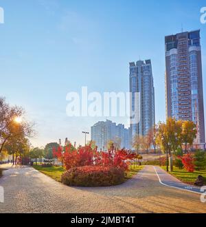 Der helle Sonnenaufgang im farbigen Natalka-Park im Herbst mit Spaziergängen, Bäumen und hohen Wohngebäuden, Obolon, Kiew, Ukraine Stockfoto