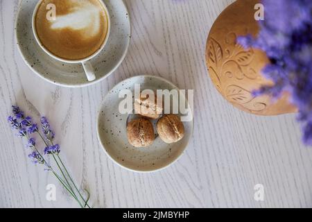 Vegane Naturnüsse Süßigkeiten ohne Zucker. Tasse Cappuccino auf einem Holztisch im Café. Natürliche Süßigkeiten. Kaffeepause. Lavendelschmuck Stockfoto