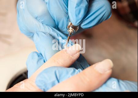 Frauenhände - der Meister in blauen Handschuhen macht den Kunden Hardware Maniküre Stockfoto