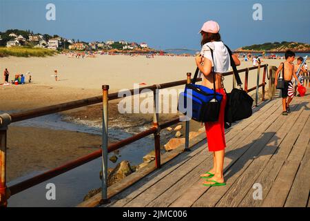 Eine Erwachsene Frau mit ihren Taschen wartet darauf, den Strand am späten Nachmittag an einem schönen sonnigen Sommerurlaubstag am Good Harbour Beach zu verlassen Stockfoto